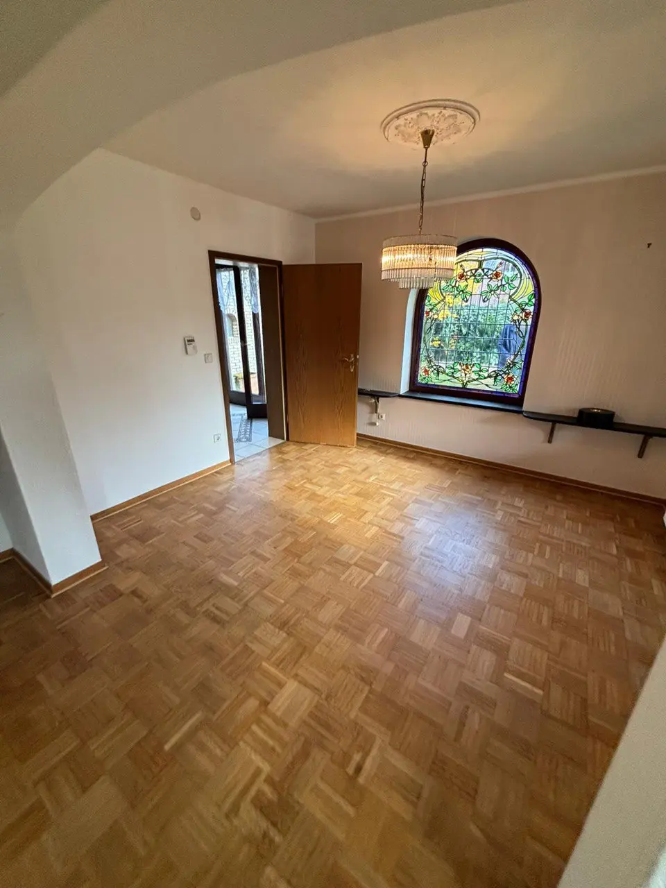 Leerer Raum mit Parkettboden und Rundbogenfenster nach der Räumung