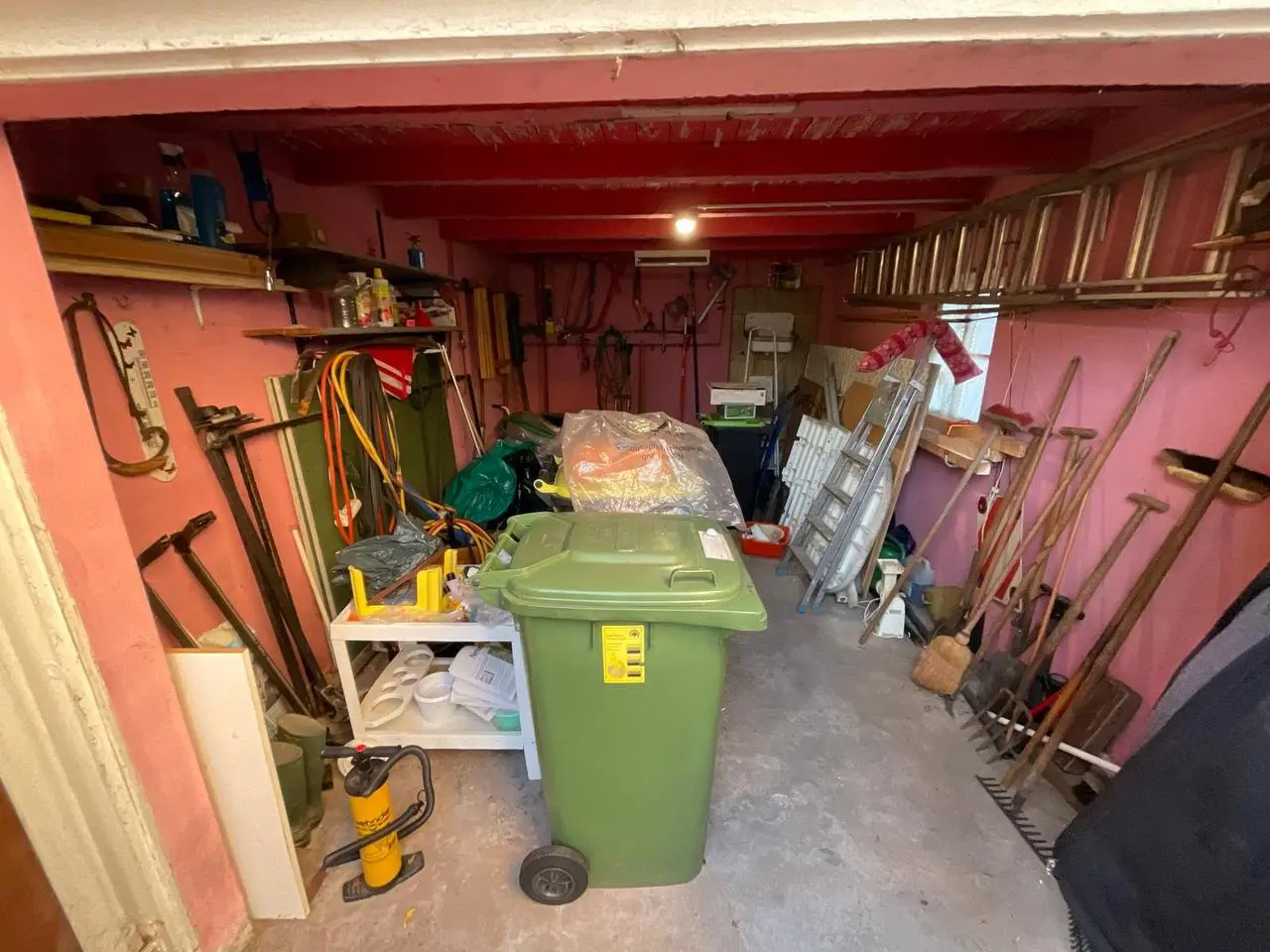 Volle Garage mit Werkzeug, Regalen und Mülltonne